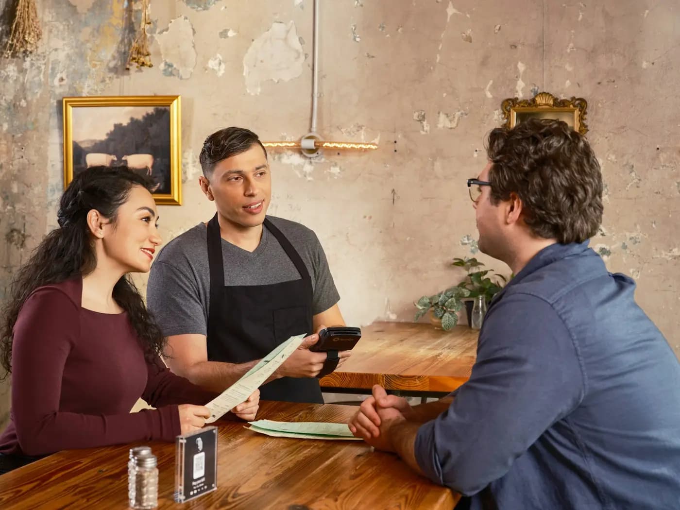 Un camarero toma nota en una tableta mientras habla con dos clientes